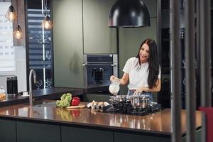 préparer des aliments en utilisant des légumes et des produits sains. jeune belle brune en vêtements décontractés à l'intérieur dans la cuisine pendant la journée photo