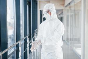 femme médecin scientifique en blouse de laboratoire, lunettes défensives et masque debout à l'intérieur et portant des gants photo