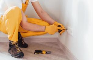 homme à tout faire en uniforme jaune travaille avec l'électricité et installe une nouvelle prise. conception de rénovation de maison photo