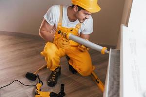 un homme à tout faire en uniforme jaune travaille à l'intérieur avec une batterie thermique à l'aide d'un outil spécial. conception de rénovation de maison photo