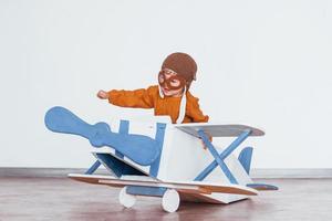 petit garçon en uniforme de pilote rétro s'amusant avec un avion jouet à l'intérieur photo