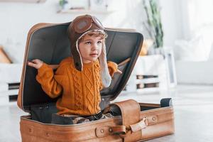 les petits garçons en costume de pilote rétro s'amusent et s'assoient dans une valise à l'intérieur pendant la journée photo