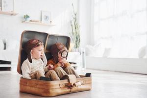 deux petits garçons s'amusent et s'assoient dans une valise à l'intérieur pendant la journée photo