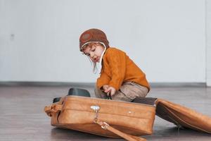 les petits garçons en costume de pilote rétro s'amusent et s'assoient dans une valise à l'intérieur pendant la journée photo