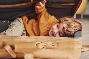 les petits garçons en costume de pilote rétro s'amusent et se couchent dans une valise à l'intérieur pendant la journée photo