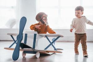 Deux petits garçons en uniforme de pilote rétro s'amusant avec un avion jouet à l'intérieur photo