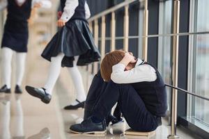 garçon en uniforme assis seul avec un sentiment de tristesse à l'école. notion de harcèlement photo