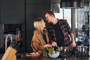 jeune couple en vêtements décontractés debout ensemble dans la cuisine et préparer la nourriture photo