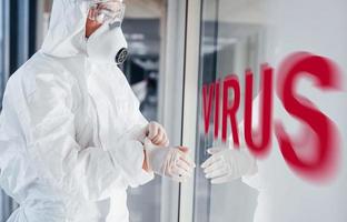 mot de virus rouge. infirmière en uniforme de protection, masque et lunettes debout à l'intérieur photo