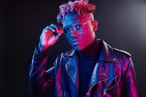 éclairage néon futuriste. jeune homme afro-américain à lunettes debout en studio photo