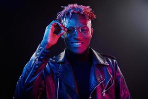éclairage néon futuriste. jeune homme afro-américain à lunettes debout en studio photo