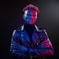 éclairage néon futuriste. jeune homme afro-américain debout en studio avec les bras croisés photo