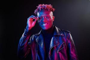 éclairage néon futuriste. jeune homme afro-américain à lunettes debout en studio photo