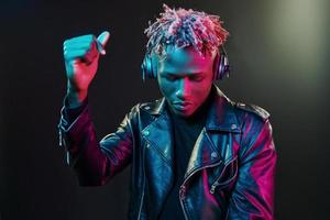 danser avec des écouteurs. éclairage néon futuriste. jeune homme afro-américain dans le studio photo