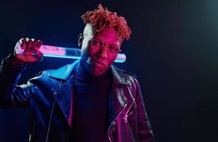 contenant du matériel d'éclairage. éclairage néon futuriste. jeune homme afro-américain à lunettes debout en studio photo