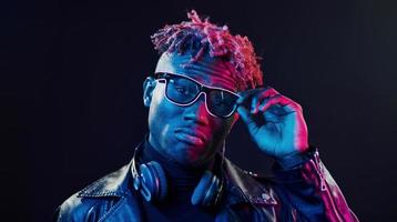 des lunettes élégantes et des écouteurs sans fil. éclairage néon futuriste. jeune homme afro-américain dans le studio photo