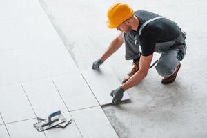 pose de plaques. homme en uniforme gris et casque orange travaille à l'intérieur dans un grand bureau moderne pendant la journée photo