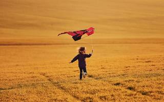 bonne petite fille qui court avec un cerf-volant dans les mains sur le beau terrain photo