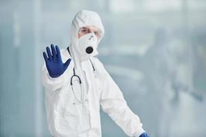 montre le geste d'arrêt à la main. homme médecin scientifique en blouse de laboratoire, lunettes défensives et masque photo