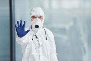 montre le geste d'arrêt à la main. homme médecin scientifique en blouse de laboratoire, lunettes défensives et masque photo