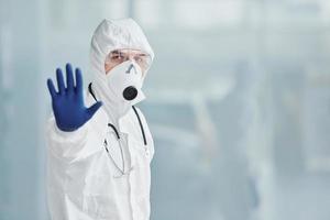 montre le geste d'arrêt à la main. homme médecin scientifique en blouse de laboratoire, lunettes défensives et masque photo