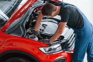 vue de dessus du travailleur masculin en uniforme qui répare l'automobile rouge photo