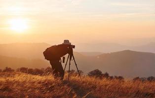 photographe masculin debout et travaillant dans un paysage majestueux d'arbres d'automne et de montagnes à l'horizon photo