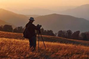 photographe masculin debout et travaillant dans un paysage majestueux d'arbres d'automne et de montagnes à l'horizon photo