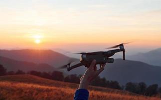 homme debout dans le champ d'automne et tient un drone à la main. Magnifique lever de soleil. paysage majestueux de montagnes lointaines photo