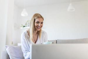 belle femme pigiste notant des informations pour la planification d'un projet faisant un travail à distance via un ordinateur portable. fille riant en lisant des e-mails sur un ordinateur portable moderne. photo