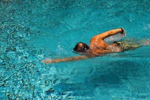 jeune homme nage dans une eau pure transparente d'une piscine par une journée ensoleillée. photo