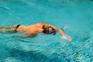 jeune homme nage dans une eau transparente d'une piscine par une journée ensoleillée. photo