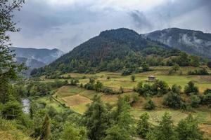 paysage de montagne d'été après la pluie avec brume, prés verts et maison rurale photo