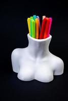 des crayons de couleur pour le dessin, situés dans un support comme un vase, se concentrent devant. crayons multicolores et feutres dans un vase en plâtre en forme de buste sur fond noir. photo