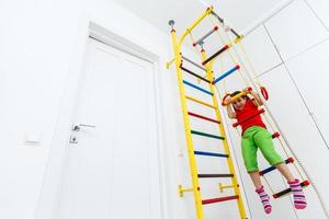 petite fille en tenue de sport faisant des exercices sur des anneaux de sport sur un mur suédois. le concept d'un mode de vie sain dès le plus jeune âge. sport des enfants. photo