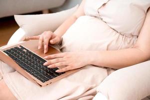 une femme enceinte utilise un ordinateur portable pour le travail, les achats en ligne, la lecture du blog ou un rendez-vous en ligne avec un médecin photo