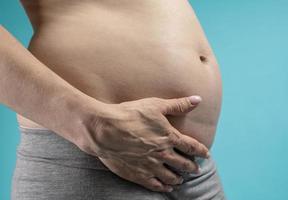 femme enceinte tient les mains sur le ventre sur un fond bleu. concept de grossesse, de maternité, de préparation et d'attente. gros plan, à l'intérieur. belle photo d'ambiance tendre de grossesse.
