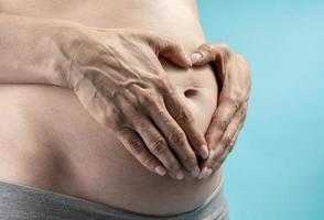 femme enceinte tient les mains sur le ventre sur un fond bleu. concept de grossesse, de maternité, de préparation et d'attente. gros plan, à l'intérieur. belle photo d'ambiance tendre de grossesse.