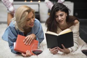 deux amies lisant un livre et buvant du vin rouge au coin du feu. concept de style de vie. photo