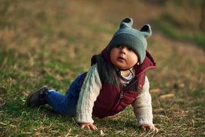 petit garçon dans des vêtements chauds allongé sur le sol du champ sur l'herbe photo