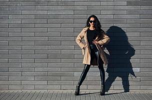 belle brune aux cheveux bouclés et en vêtements noirs à l'extérieur près du mur photo