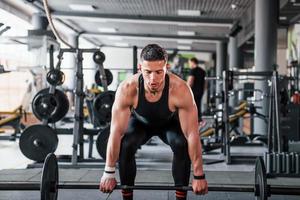 haltère de levage. jeune homme fort sportif en vêtements noirs ont une journée d'entraînement dans la salle de gym photo