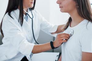 à l'aide d'un stéthoscope. une jeune femme rend visite à une femme médecin dans une clinique moderne photo