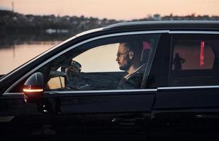 vue latérale d'un bel homme non rasé dans des vêtements à la mode qui conduit son automobile photo