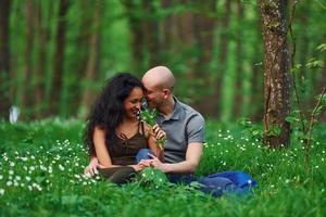 couple heureux assis sur l'herbe ensemble dans la forêt pendant la journée photo