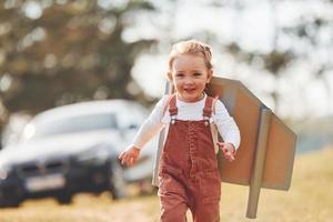 jolie petite fille avec des ailes faites à la main courant à l'extérieur sur le terrain et s'amusant photo