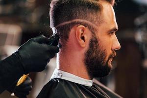 jeune homme barbu assis et se coupe les cheveux dans un salon de coiffure photo