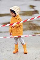 enfant en cape imperméable jaune et bottes jouant à l'extérieur près du ruban de protection après la pluie photo
