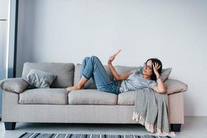 belle jeune femme en tenue décontractée allongée seule à la maison avec un smartphone dans les mains photo