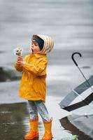 tenant des fleurs. enfant en cape imperméable jaune, bottes et parapluie jouant à l'extérieur après la pluie photo